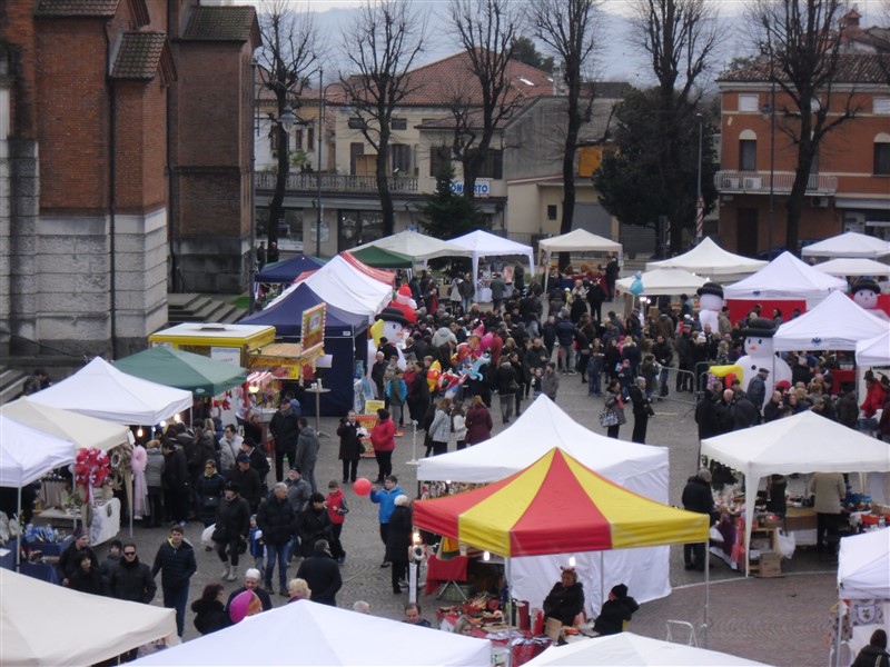 Piazza Monza gremita di bancarelle per il mercatino. Sotto, foto di gruppo per alcuni volontari della Delegazione