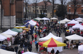 Piazza Monza gremita di bancarelle per il mercatino. Sotto, foto di gruppo per alcuni volontari della Delegazione